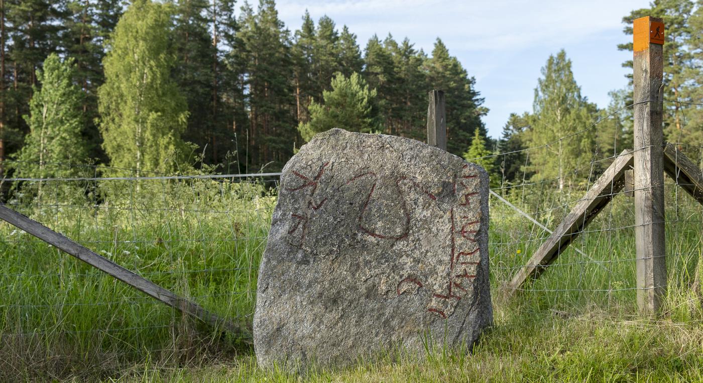 En stor runsten som ligger mitt på ett fält.