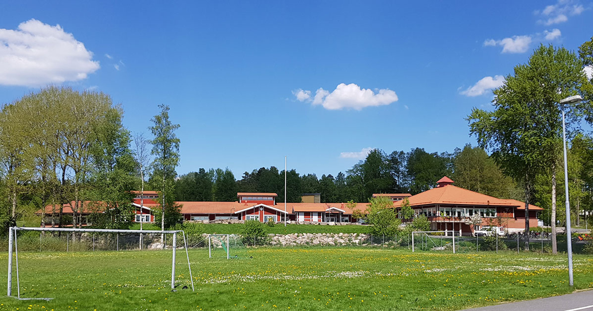 En fotbollsplan med ett fotbollsmål och med skolans byggnader i bakgrunden.