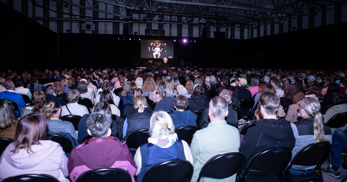 En man står på en scen och håller föredrag framför en stor, sittande publik.