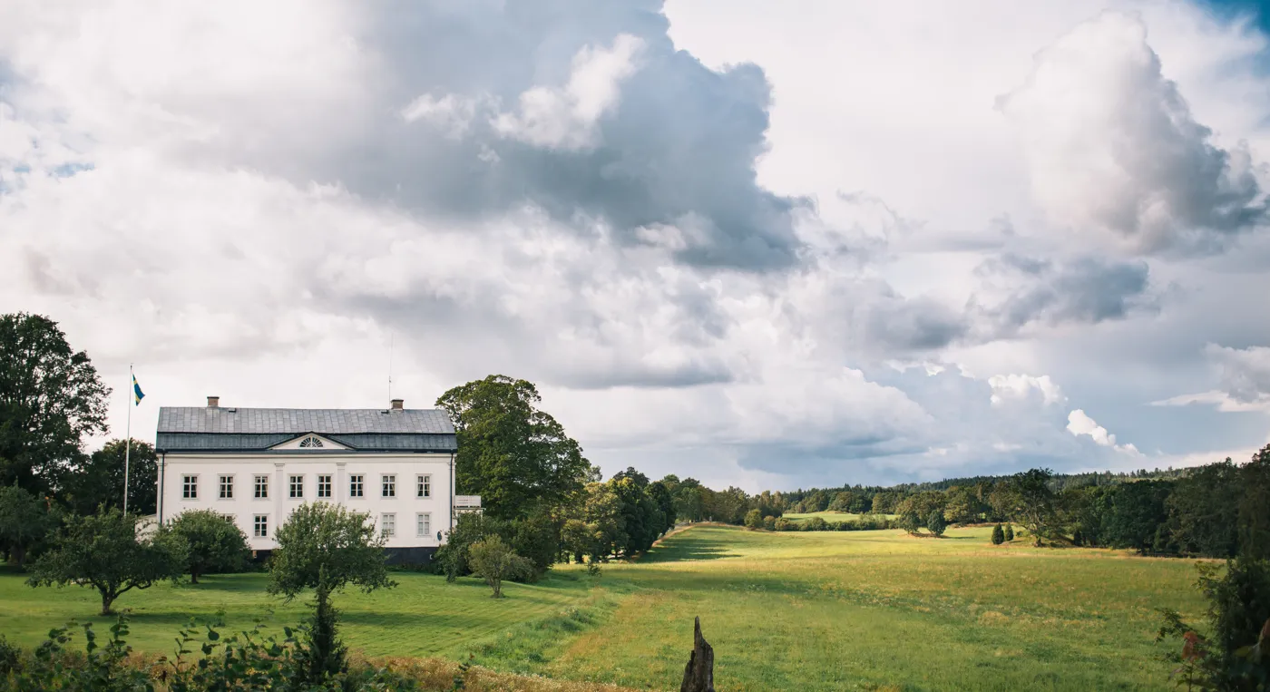Ett stort vitt hus som ligger på toppen av en frodig grön äng.