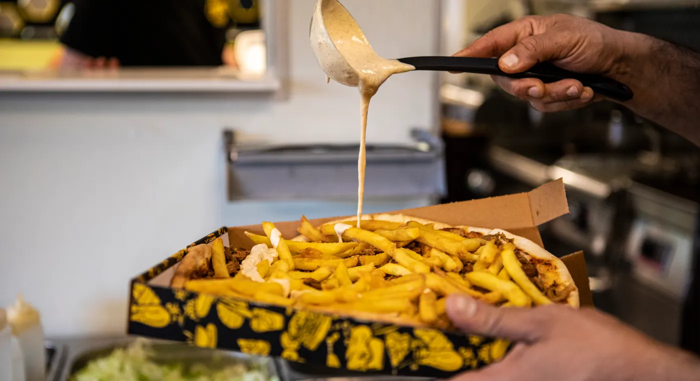 En person som häller sås över en pizza med pommes på.