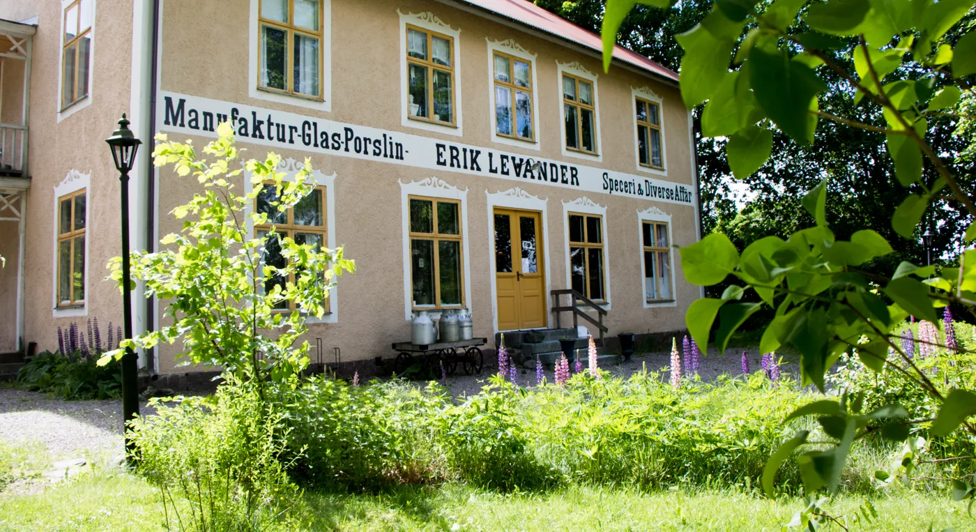 En gammal byggnad med putsad fasad och en bord med texten manufaktur, glas, porslin, Erik Lewander, speceri och diverseaffär.