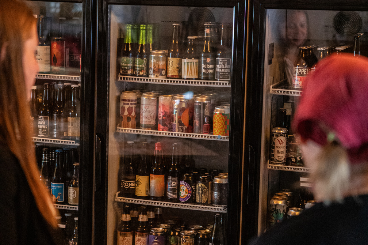 Två personer står framför en rad kylskåp med olika ölsorter i.