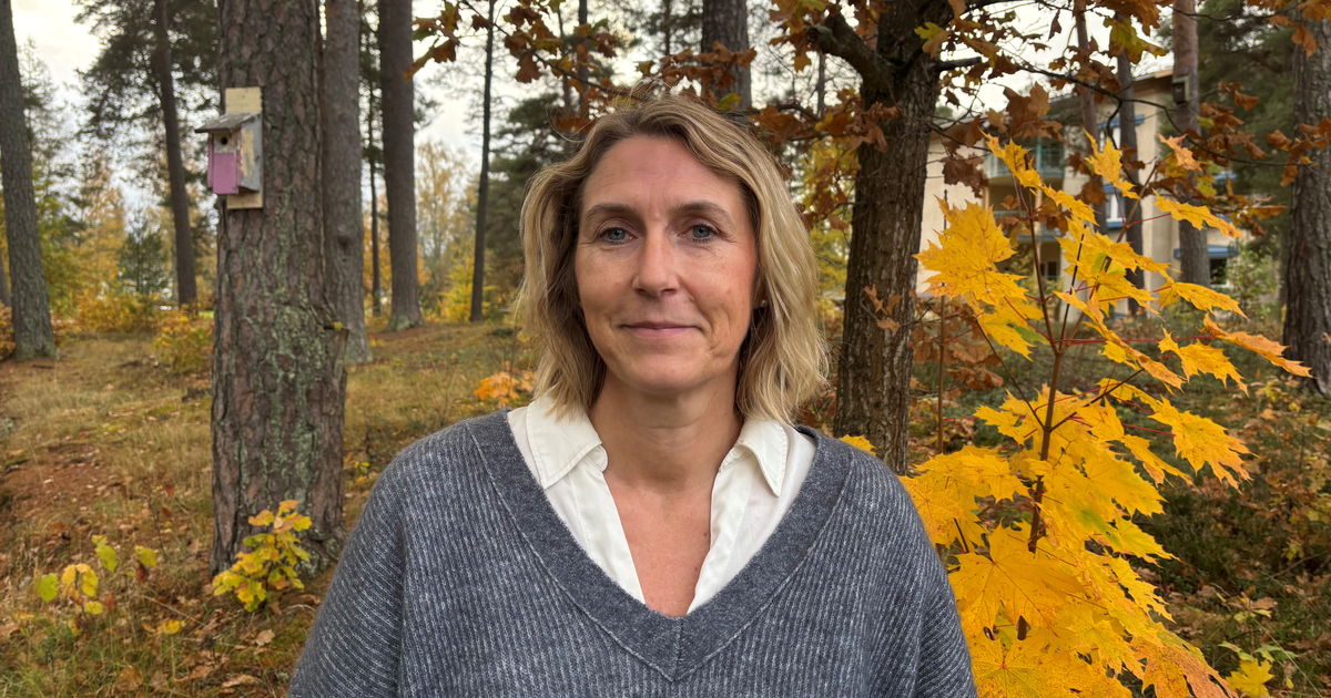 Kvinna med ljust hår står utomhus med träd i bakgrunden.