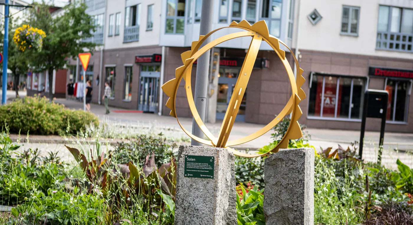 En skulptur föreställande en sol i en offentlig plantering.