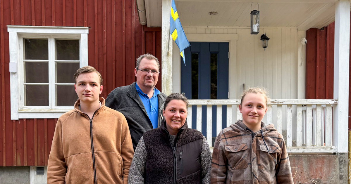 Familjen, två söner, mamma och pappa, uppställda framför det röda huset.