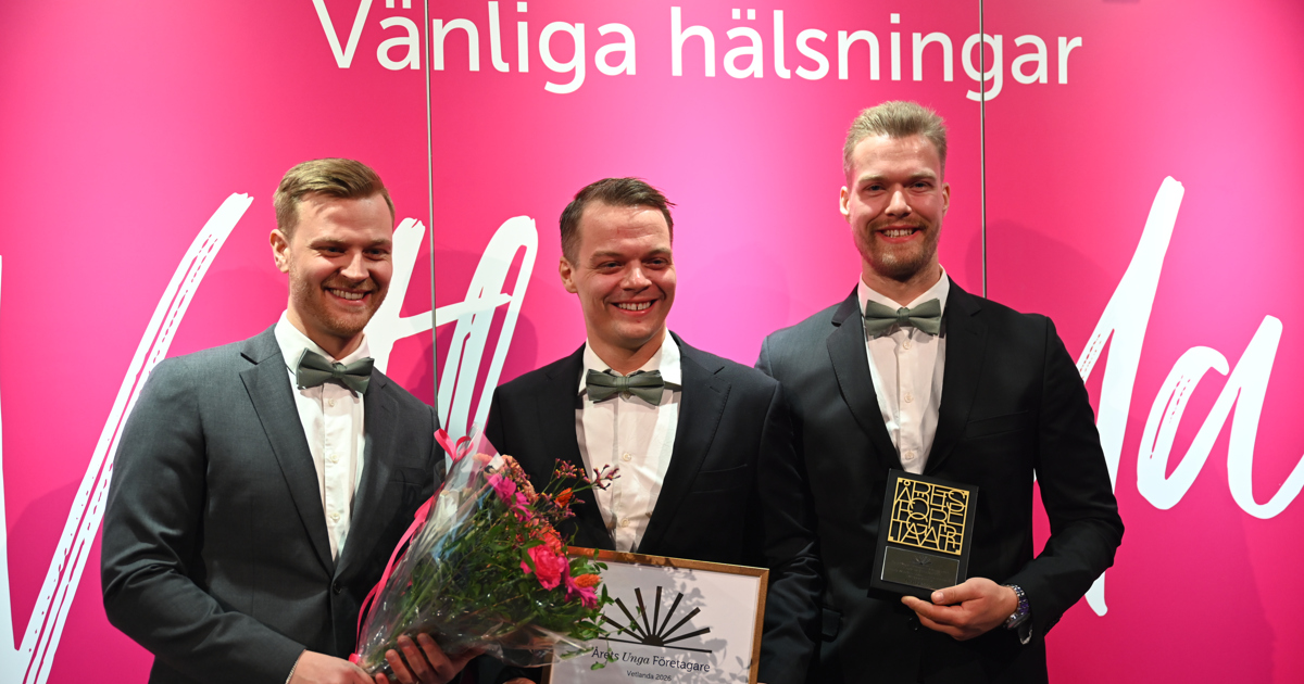 De tre killarna bakom SW Elservice står framför en fotovägg med blombukett, diplom och en statyett.