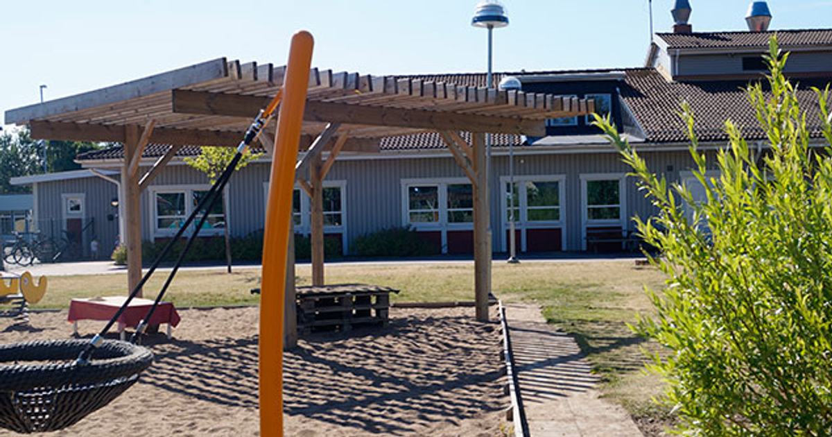 En lekplats för barn med gungor. Förskolans byggnad syns i bakgrunden.